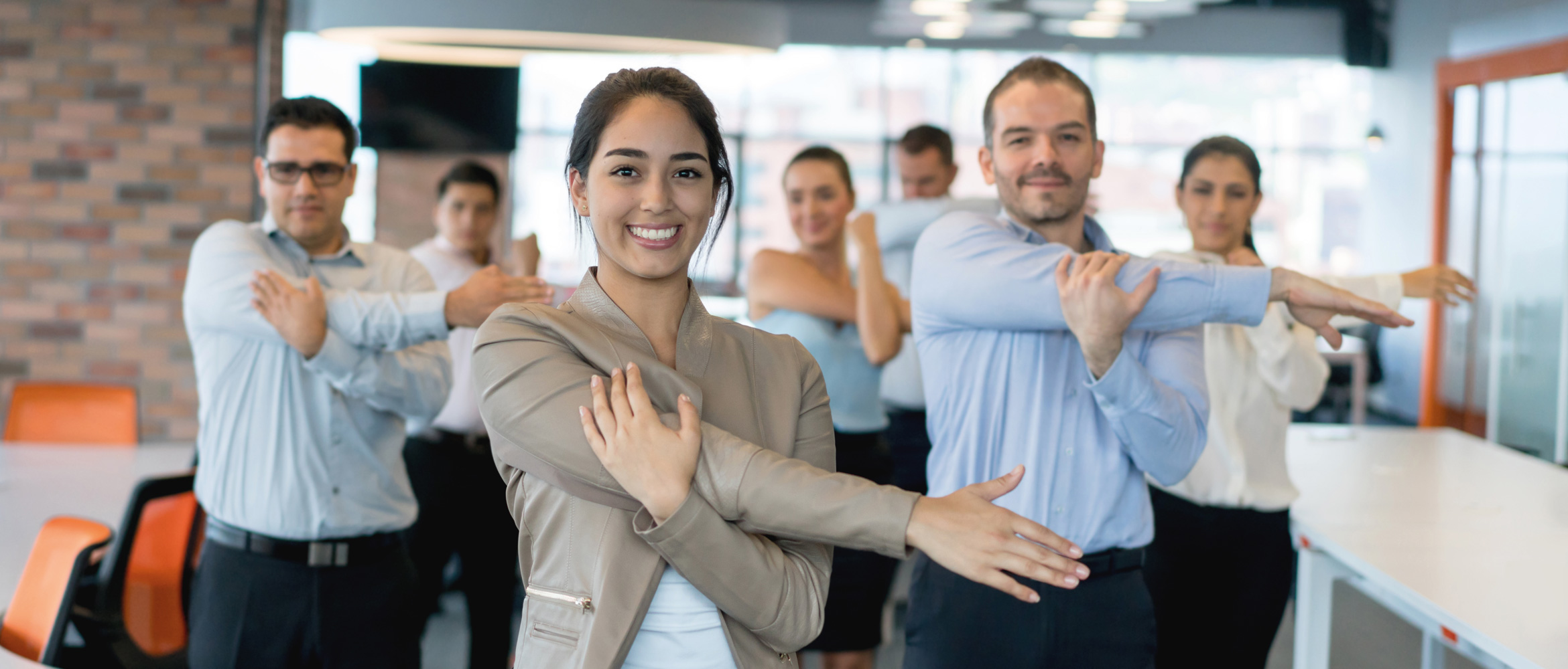 Sept employés de bureau habillés en business casual, quatre hommes et trois femmes, font de l’exercice, ici un étirement des bras.