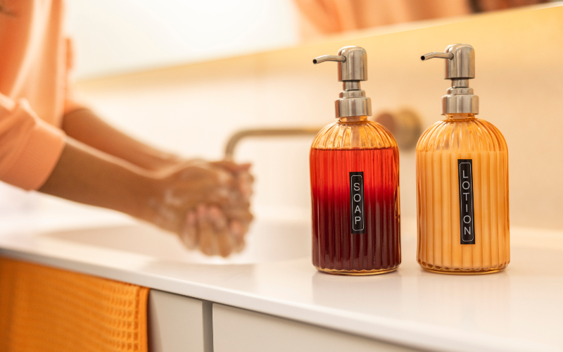 Woman washing her hands in the sink with two bottles next to it with labels