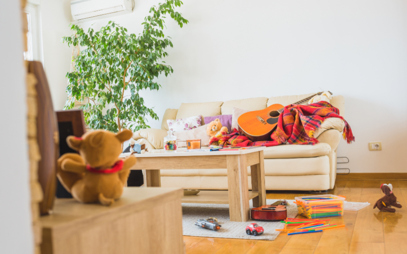 Messy lounge with a sofa, floor and table covered with a guitar, toys, and teddy bear
