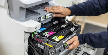 Two hands opening a printer which shows three toner cartridges