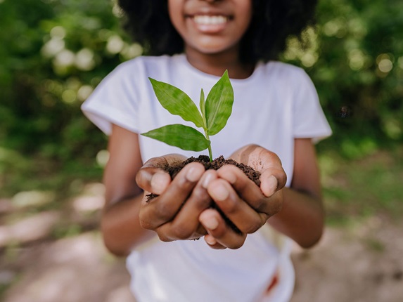 Girl in white tshirt hold a green tree shoot in her cupped hands