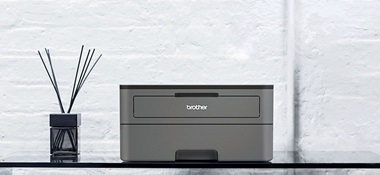 Dunkelgrauer Schwarzweiss-Laserdrucker HL-2350DW auf einem Glastisch mit Diffusor
