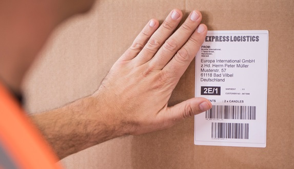 Man in orange high-vis jacket placing a delivery label on a cardboard box