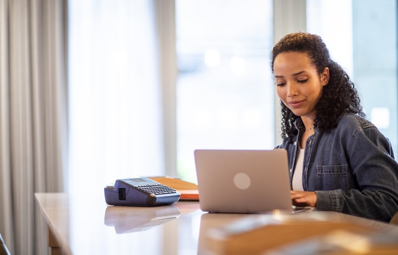 Woman sitting in coworking space with PT-D410 label printer and laptop 