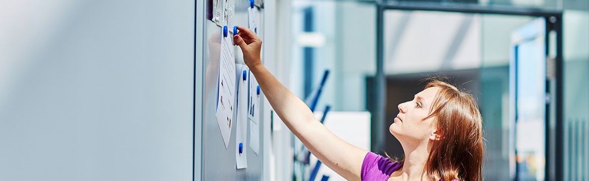 Woman in purple shirt pinning a poster to a notice board 